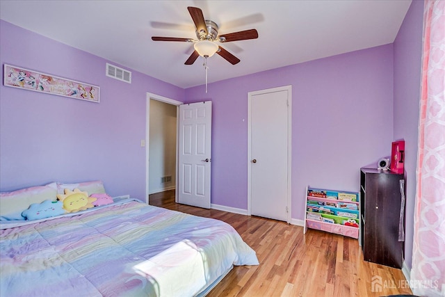 bedroom with a ceiling fan, wood finished floors, visible vents, and baseboards