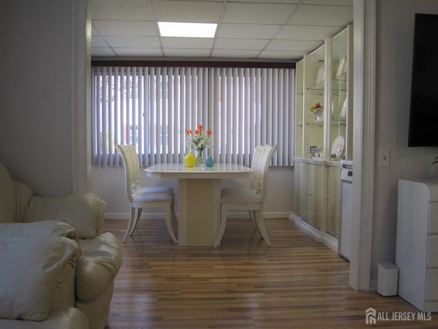 dining space featuring light wood-type flooring, a paneled ceiling, and baseboards