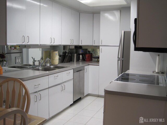 kitchen with stainless steel appliances, light tile patterned flooring, a sink, and white cabinets