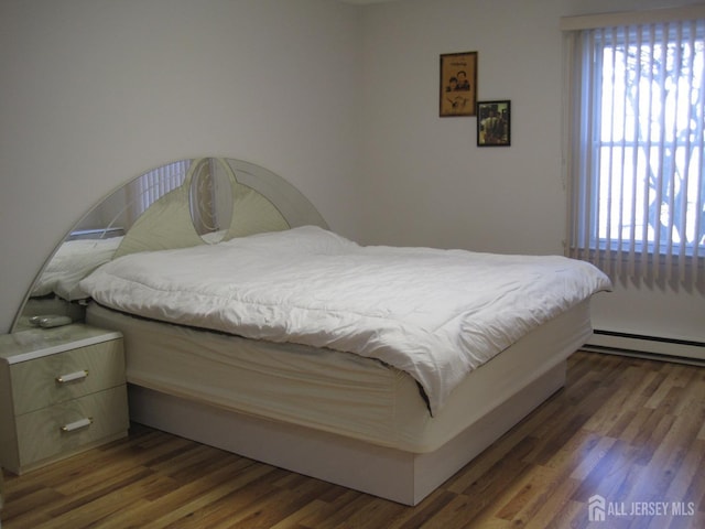 bedroom featuring multiple windows, a baseboard heating unit, and wood finished floors