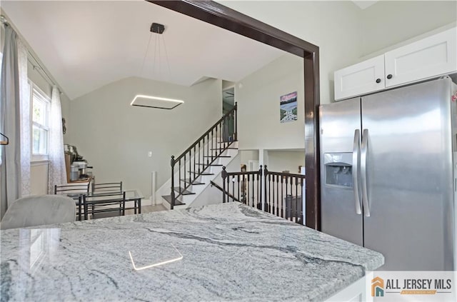 kitchen featuring stainless steel fridge, white cabinetry, vaulted ceiling, light stone counters, and hanging light fixtures