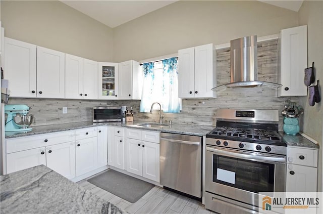 kitchen with stainless steel appliances, wall chimney range hood, a sink, tasteful backsplash, and vaulted ceiling