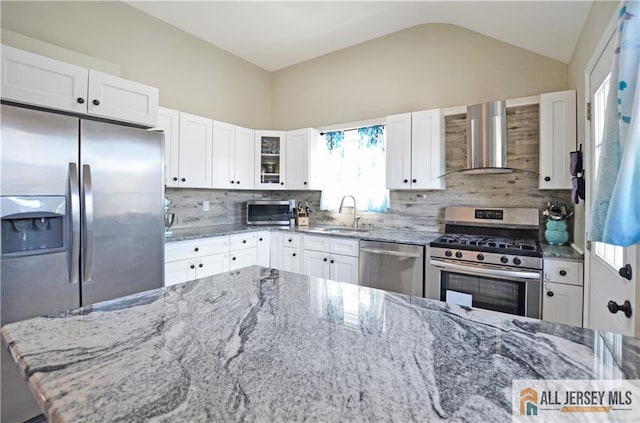 kitchen featuring wall chimney range hood, stainless steel appliances, a sink, decorative backsplash, and vaulted ceiling