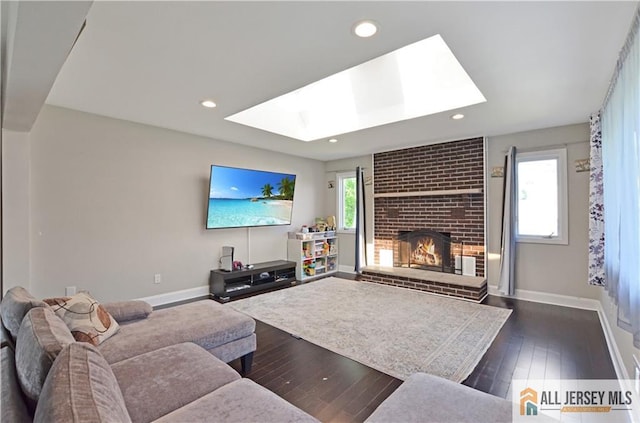 living area with a skylight, a fireplace, baseboards, dark wood-style flooring, and recessed lighting