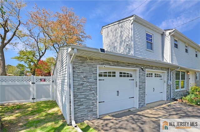 view of property exterior featuring fence, a garage, stone siding, and driveway