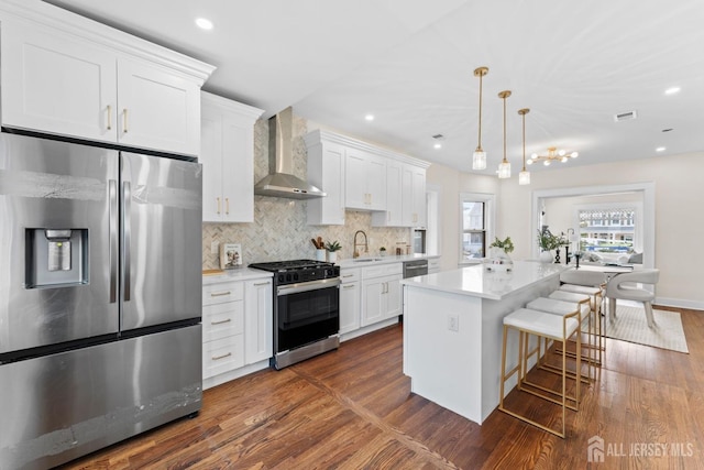 kitchen featuring a sink, stainless steel appliances, light countertops, dark wood-type flooring, and wall chimney range hood