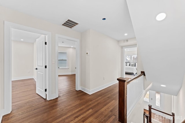 hallway with an upstairs landing, visible vents, dark wood-type flooring, and baseboards