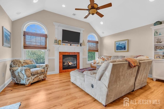living area with vaulted ceiling, ceiling fan, a glass covered fireplace, and light wood finished floors