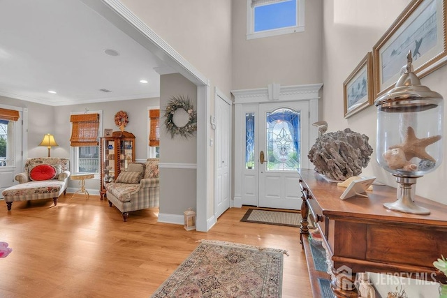 foyer entrance with crown molding, baseboards, a towering ceiling, light wood-style floors, and recessed lighting