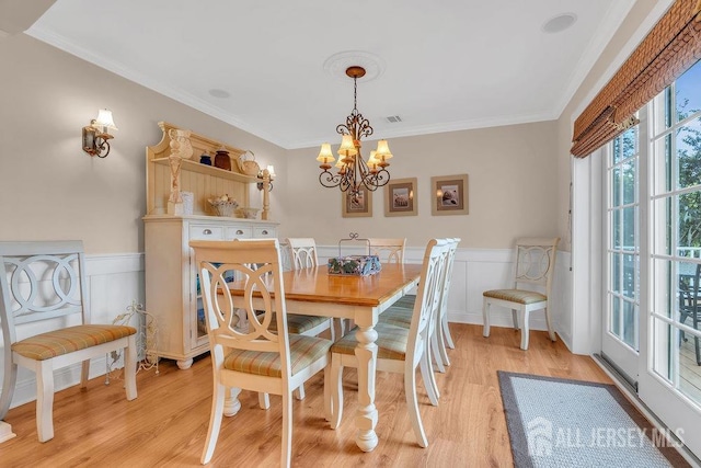 dining area featuring wainscoting, a chandelier, ornamental molding, and light wood-style flooring