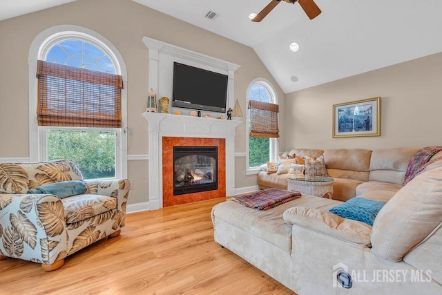 living room featuring lofted ceiling, a ceiling fan, a glass covered fireplace, visible vents, and wood finished floors