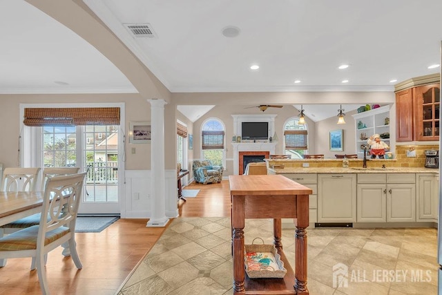 kitchen with a peninsula, ornate columns, a fireplace, crown molding, and arched walkways