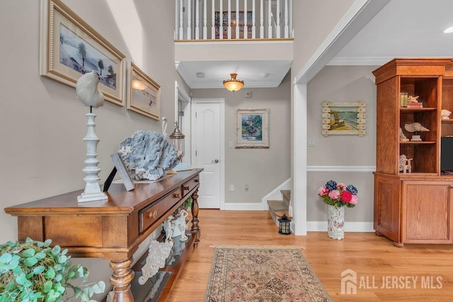 foyer entrance featuring ornamental molding, light wood-style flooring, stairs, and baseboards