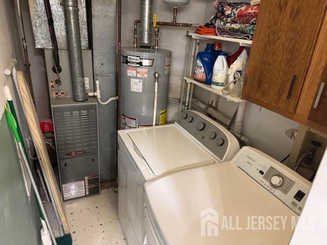 clothes washing area featuring washer and dryer, gas water heater, and cabinet space