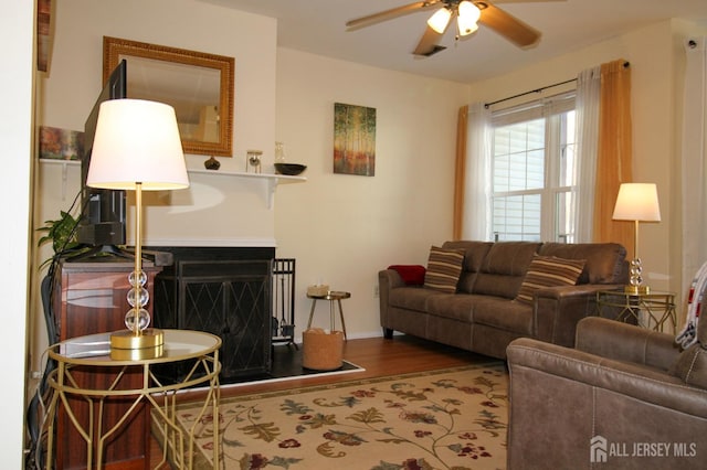 living area featuring ceiling fan, a fireplace, wood finished floors, and baseboards