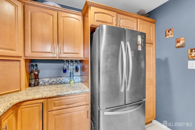 kitchen featuring baseboards, tasteful backsplash, freestanding refrigerator, and light stone countertops