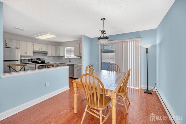 dining space with light hardwood / wood-style flooring, sink, a baseboard radiator, and a textured ceiling