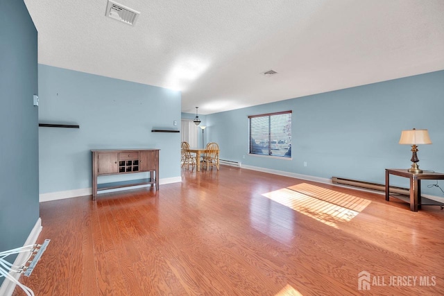 living room with hardwood / wood-style flooring, baseboard heating, and a textured ceiling