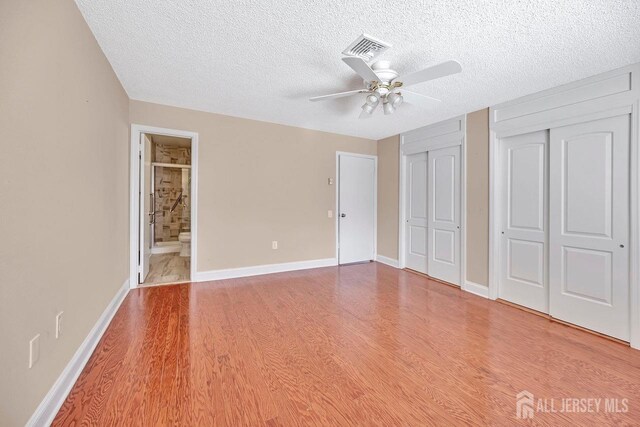 unfurnished bedroom featuring connected bathroom, a textured ceiling, multiple closets, hardwood / wood-style flooring, and ceiling fan