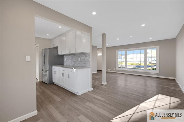 kitchen with tasteful backsplash, freestanding refrigerator, white cabinetry, and wood finished floors