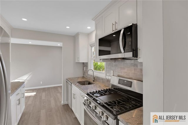 kitchen featuring light stone counters, a sink, white cabinets, appliances with stainless steel finishes, and backsplash