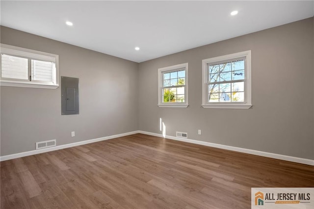 unfurnished room featuring baseboards, electric panel, visible vents, and wood finished floors