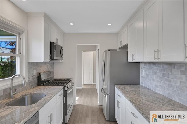 kitchen with light stone countertops, white cabinetry, stainless steel appliances, and a sink