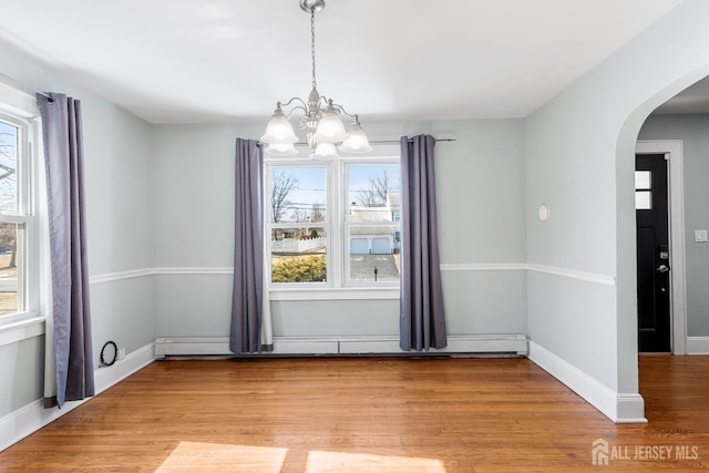 unfurnished dining area with arched walkways, a notable chandelier, light wood finished floors, baseboard heating, and baseboards