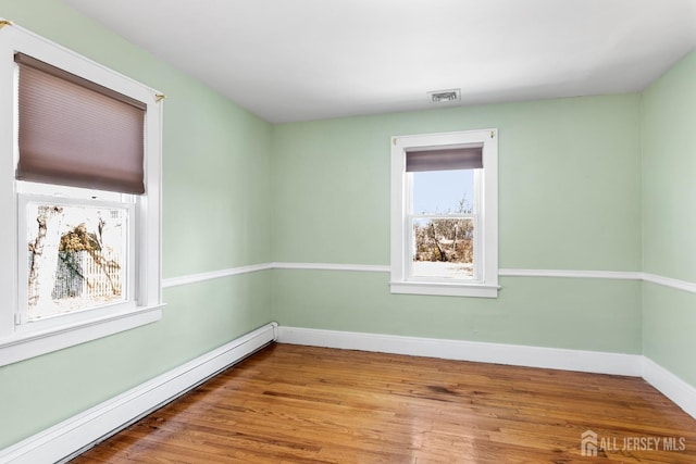 spare room featuring a baseboard radiator, visible vents, baseboards, and wood finished floors