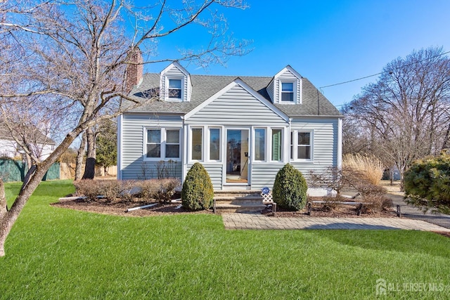 cape cod home with roof with shingles, a chimney, and a front lawn