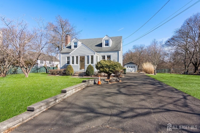 cape cod house featuring driveway, a garage, a chimney, an outdoor structure, and a front lawn