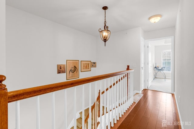 corridor featuring wood-type flooring, an upstairs landing, and baseboards