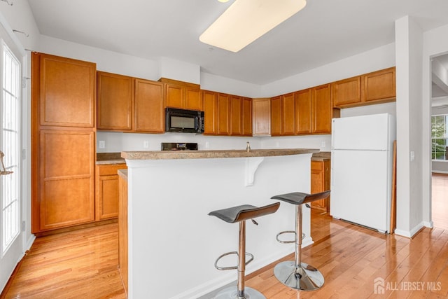 kitchen featuring electric range oven, a kitchen bar, black microwave, light wood-style flooring, and freestanding refrigerator