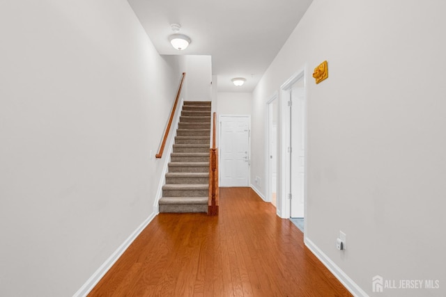 corridor with stairs, wood finished floors, and baseboards