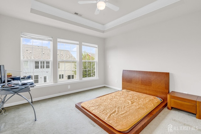 carpeted bedroom with a ceiling fan, visible vents, baseboards, and a tray ceiling