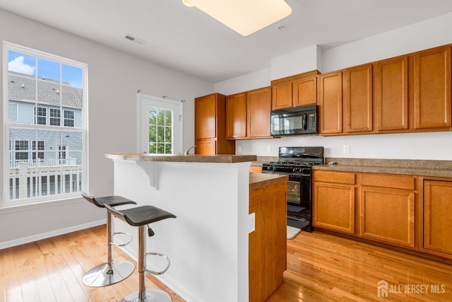 kitchen featuring a breakfast bar area, brown cabinetry, black appliances, and light wood-style floors