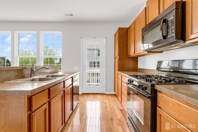 kitchen with a sink, visible vents, black appliances, light wood finished floors, and brown cabinetry