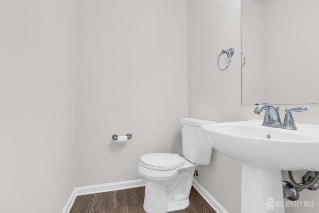 half bath with a sink, wood finished floors, toilet, and baseboards
