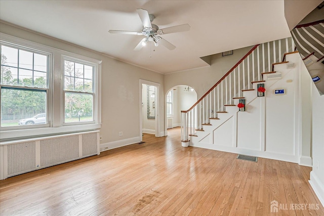foyer entrance with radiator heating unit, stairs, light wood-style flooring, arched walkways, and a ceiling fan
