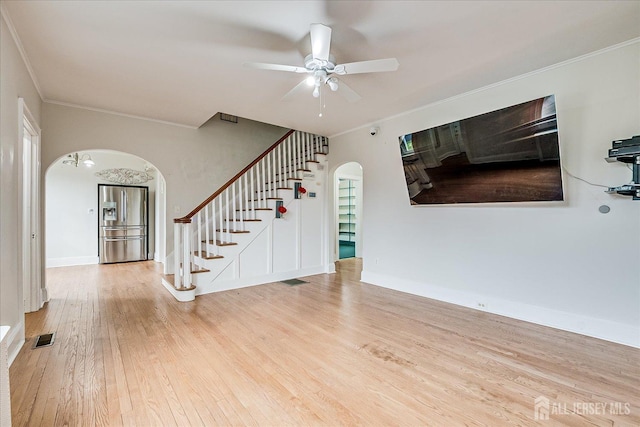 unfurnished living room featuring arched walkways, stairs, crown molding, wood finished floors, and ceiling fan