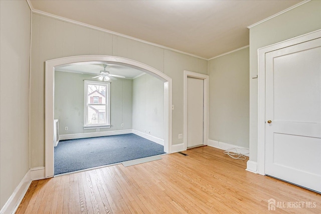 spare room with arched walkways, ornamental molding, hardwood / wood-style floors, ceiling fan, and baseboards