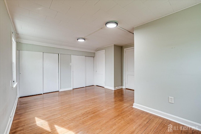 unfurnished bedroom with light wood-type flooring, baseboards, and two closets