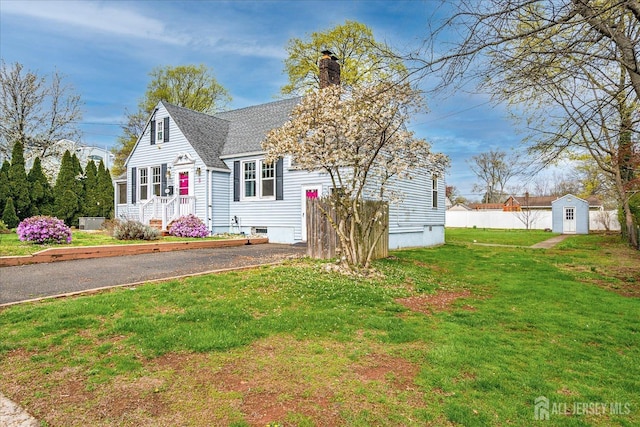 bungalow-style house featuring a storage shed, a chimney, a front lawn, an outbuilding, and a shingled roof