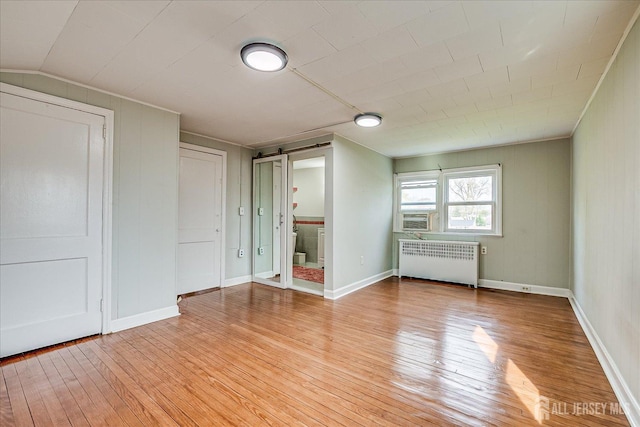 unfurnished bedroom with radiator, light wood-type flooring, a barn door, and cooling unit
