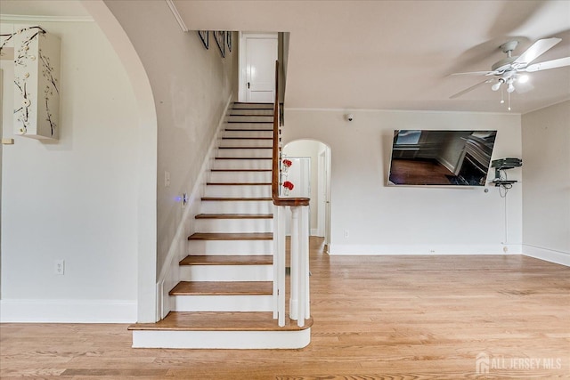 stairs with arched walkways, a ceiling fan, wood finished floors, and baseboards