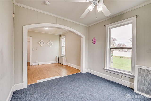empty room featuring arched walkways, radiator, ornamental molding, a ceiling fan, and a smoke detector