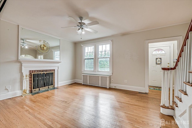 unfurnished living room with radiator heating unit, a ceiling fan, stairway, light wood-type flooring, and ornamental molding
