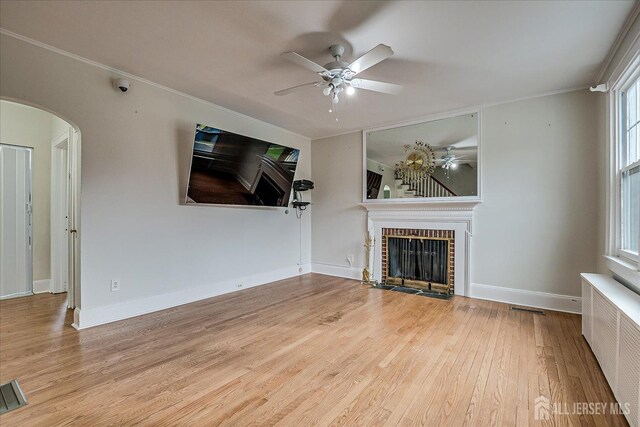 unfurnished living room with a ceiling fan, radiator heating unit, arched walkways, a fireplace, and wood finished floors