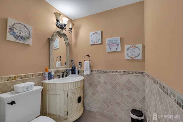 half bath featuring tile patterned floors, wainscoting, tile walls, and toilet