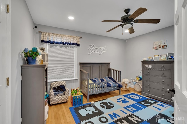 bedroom with recessed lighting, a crib, a ceiling fan, and wood finished floors